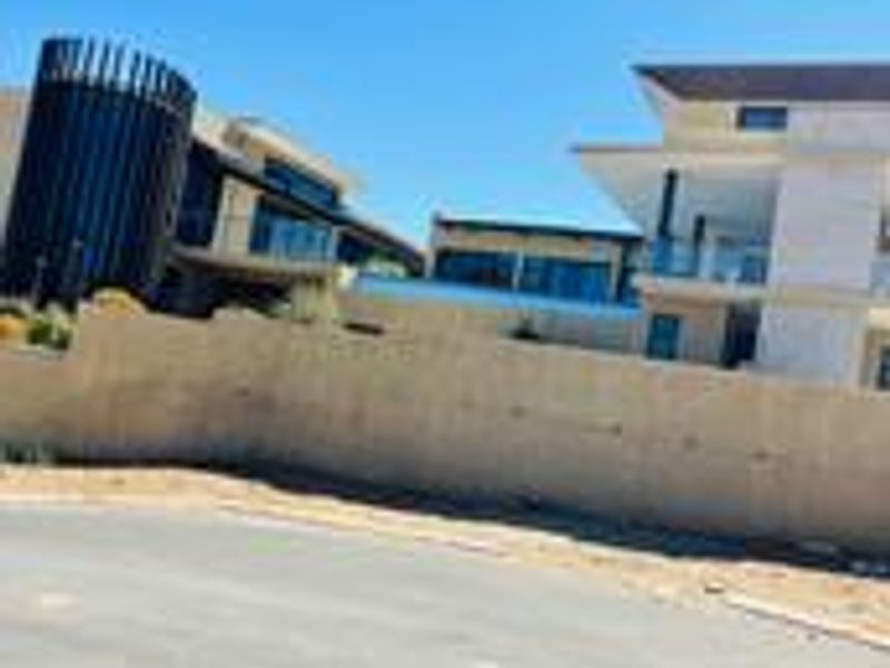 Street view showing modern residential properties with contemporary architectural design, glass balustrades, and a perimeter boundary wall.