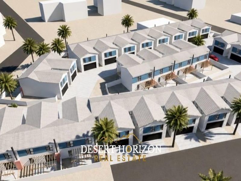An aerial perspective of a modern townhouse development featuring uniform pitched roofs, paved driveways, and integrated garage access within a landscaped estate.