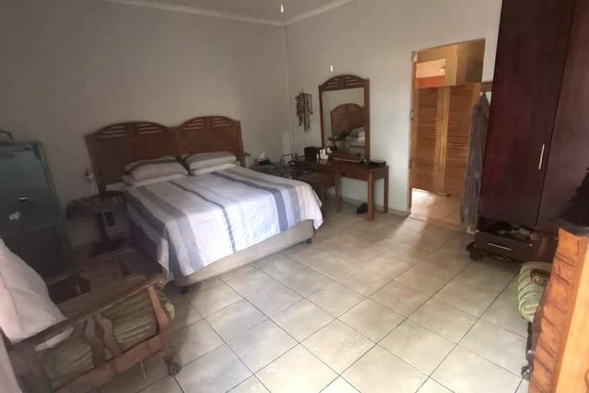 A spacious bedroom featuring tiled flooring, a ceiling fan, and an adjoining en-suite bathroom.