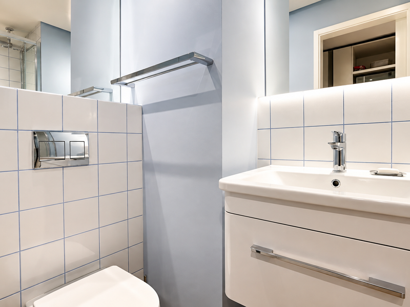 Modern bathroom featuring a wall-mounted toilet with chrome flush plate, vanity basin with mixer tap, and tiled finishes.