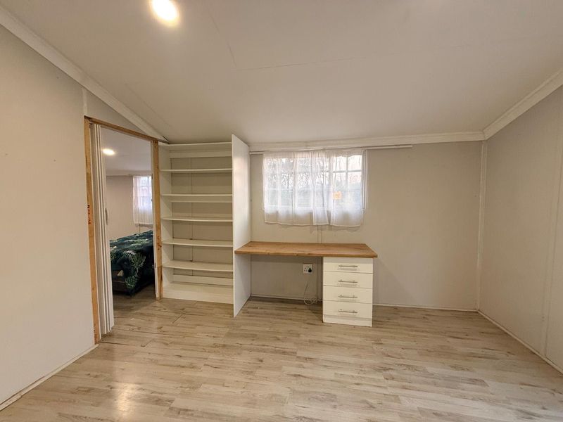 A bedroom featuring light laminate flooring, built-in shelving, and a desk area, with an adjacent room visible through an unfinished doorway.