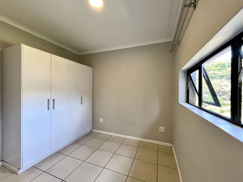 A clean, empty bedroom featuring neutral tiled flooring, a large built-in wardrobe, and a window providing natural light.