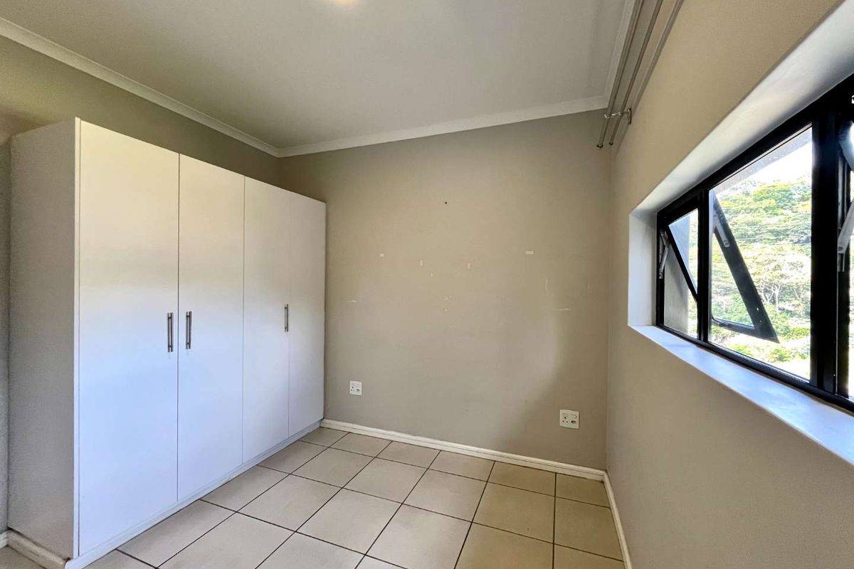 A clean, empty bedroom featuring neutral tiled flooring, a large built-in wardrobe, and a window providing natural light.