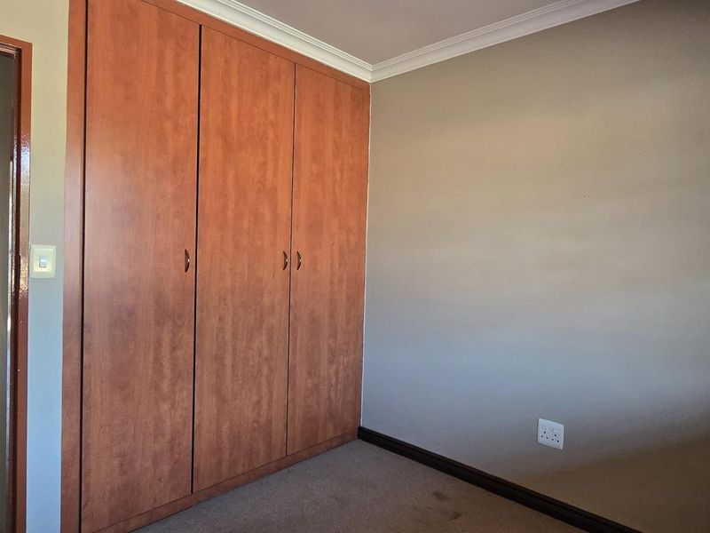 A vacant bedroom featuring built-in wooden cupboards, neutral wall finishes, and carpeted flooring, with a view into the adjacent hallway.