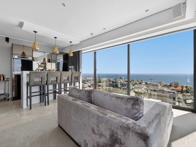 Modern open-plan living area featuring a sleek built-in bar and expansive floor-to-ceiling windows offering panoramic coastal and city views.