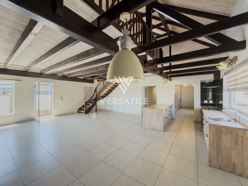 Spacious open-plan living area featuring exposed timber beams, a modern kitchen with island, and a timber staircase leading to a mezzanine level.