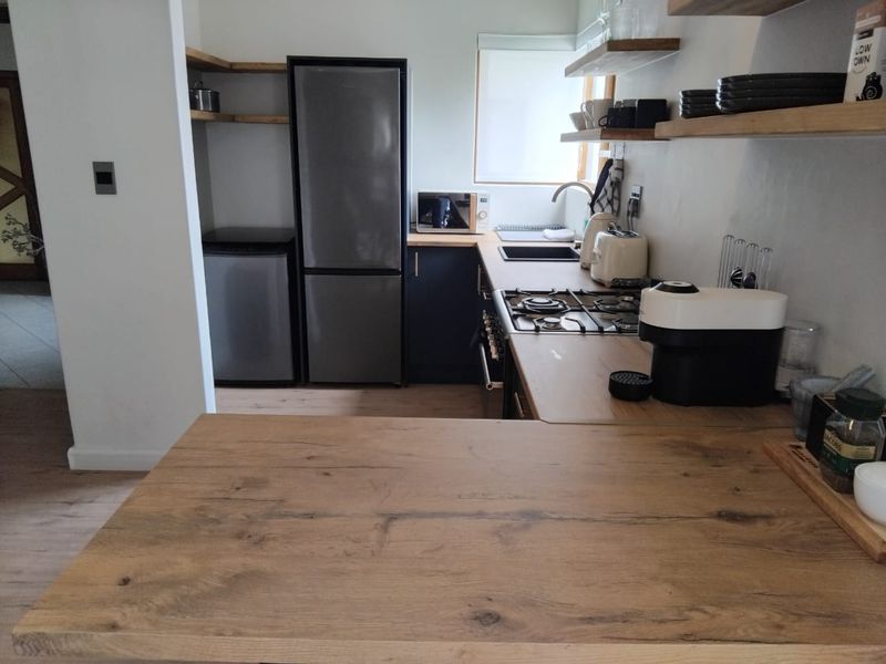Modern kitchen featuring dark cabinetry, timber floating shelves, laminate wood countertops, and a built-in gas hob with an integrated oven.
