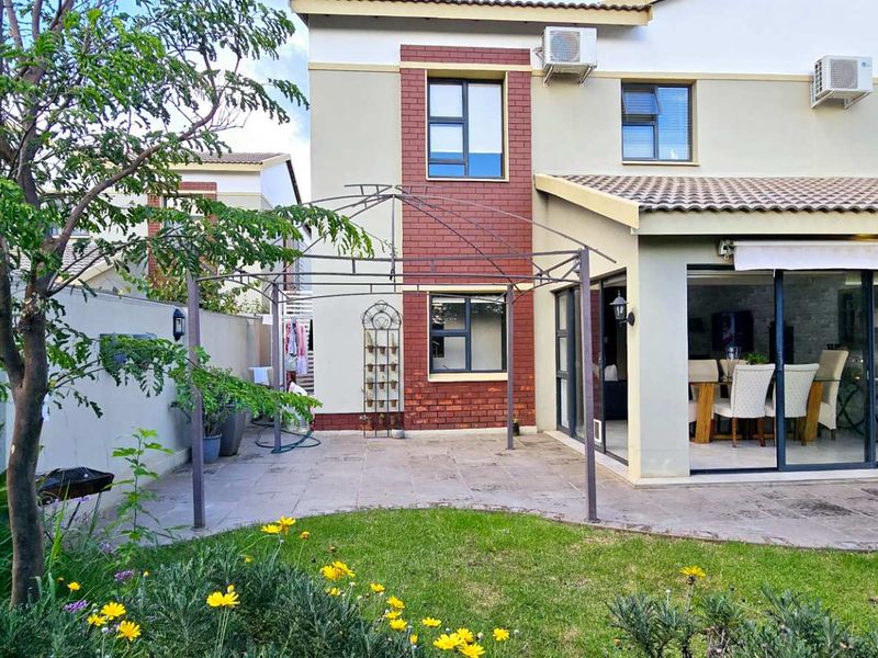 Rear view of the townhouse featuring a paved patio area, landscaped garden, and sliding glass doors leading into the living space.