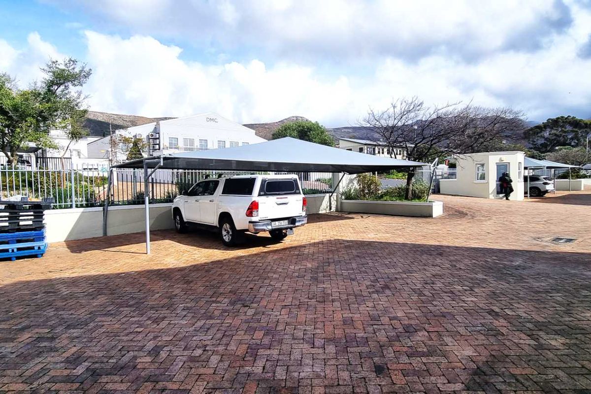Exterior view of a paved office parking area featuring covered shade-net parking bays and perimeter security fencing.