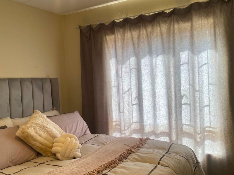 A bedroom featuring a neutral wall finish and a window dressed with curtains.