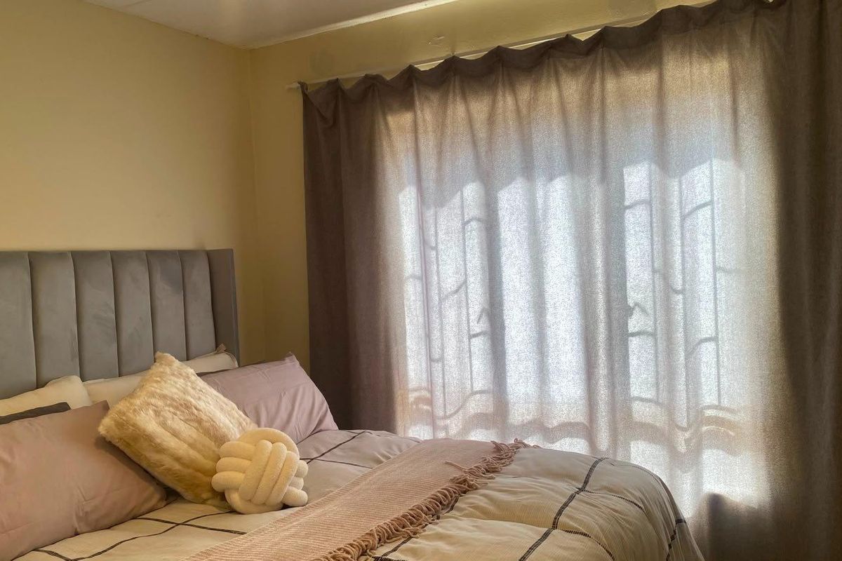 A bedroom featuring a neutral wall finish and a window dressed with curtains.