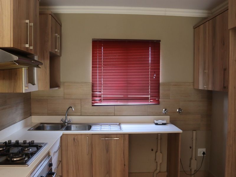A functional kitchen featuring wood-look cabinetry, a stainless steel sink, gas hob, and tiled splashback, with dedicated space for under-counter appliances.