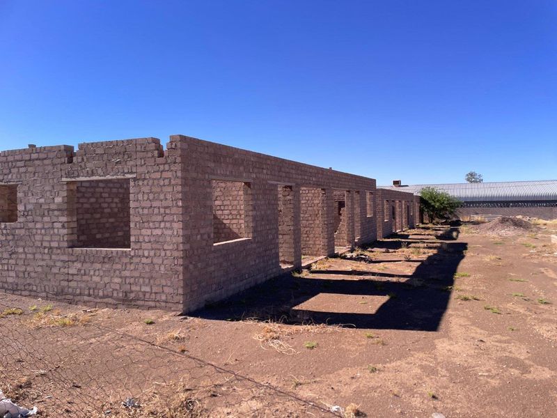 An unfinished brick structure in the early stages of construction, featuring open window and door frames on a vacant plot.