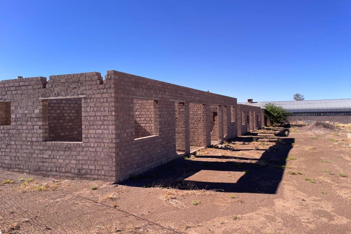 An unfinished brick structure in the early stages of construction, featuring open window and door frames on a vacant plot.