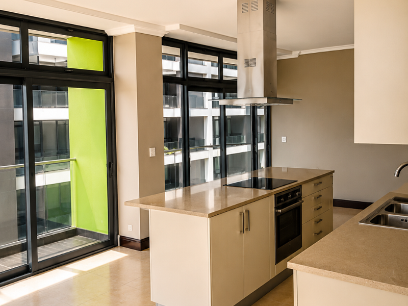 Modern open-plan kitchen featuring a central island with built-in oven and hob, stone countertops, and large sliding doors leading to a balcony.
