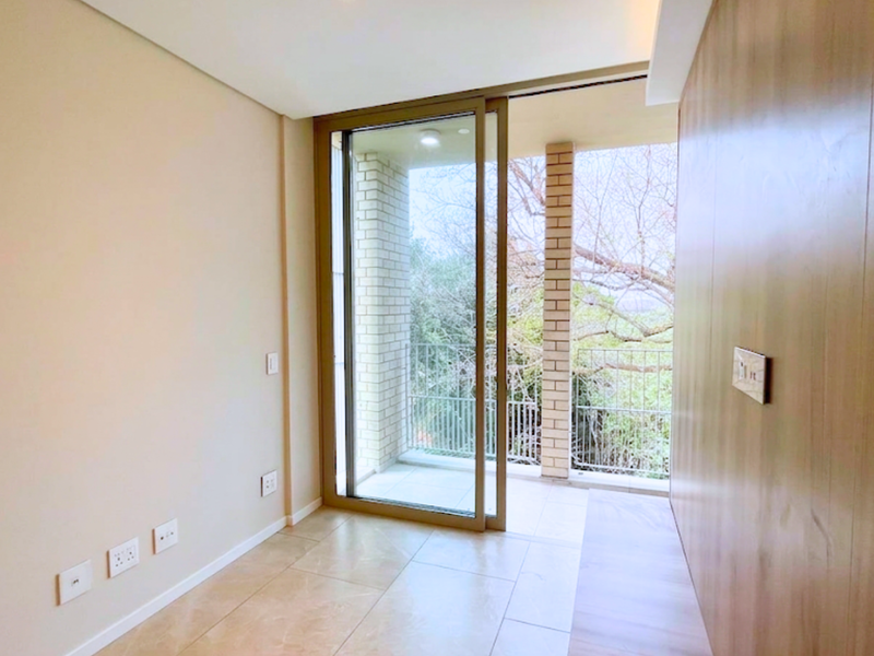 A bright, modern, and empty living area featuring wood-paneled walls, tiled floors, and a large sliding glass door leading to a private balcony.