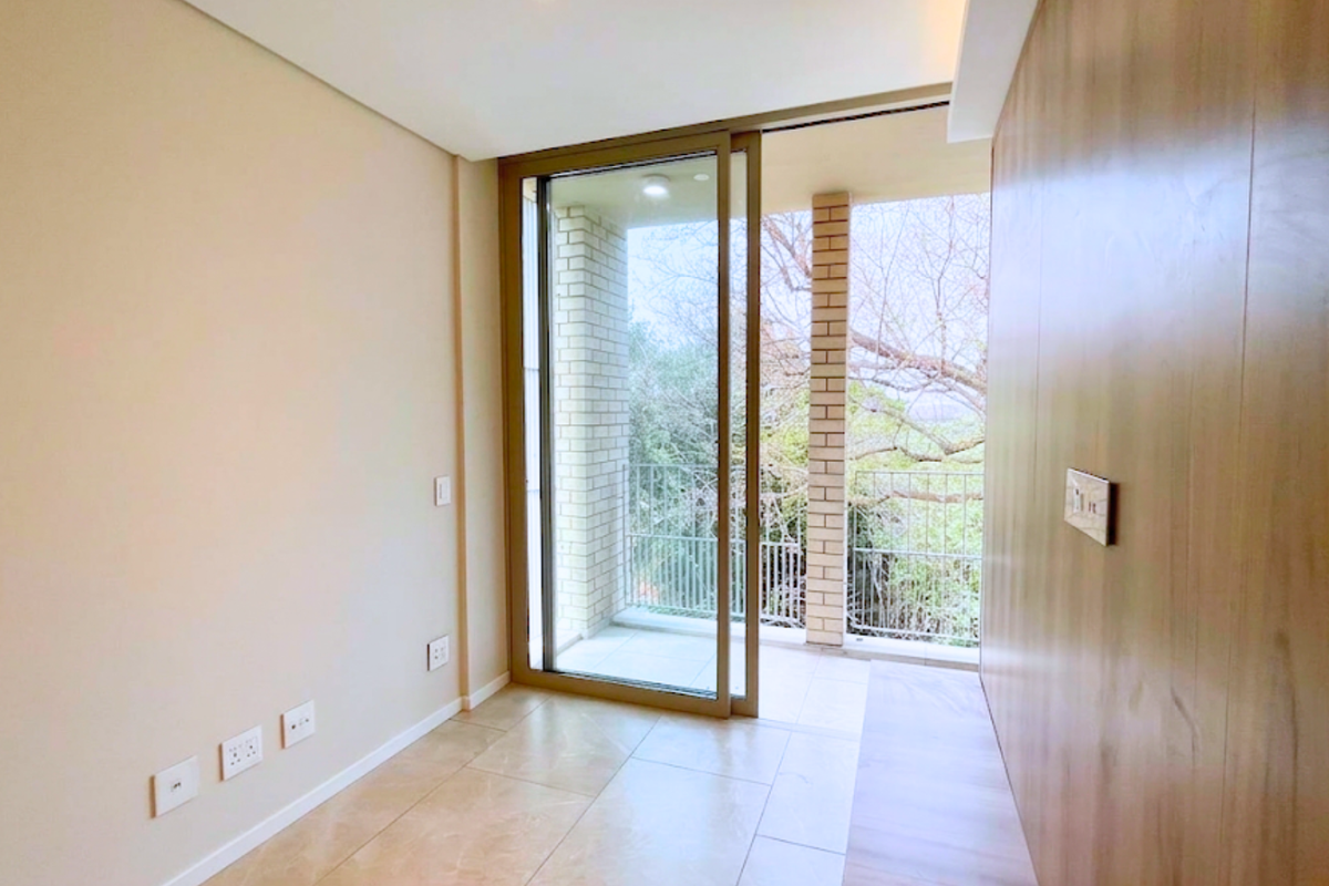 A bright, modern, and empty living area featuring wood-paneled walls, tiled floors, and a large sliding glass door leading to a private balcony.