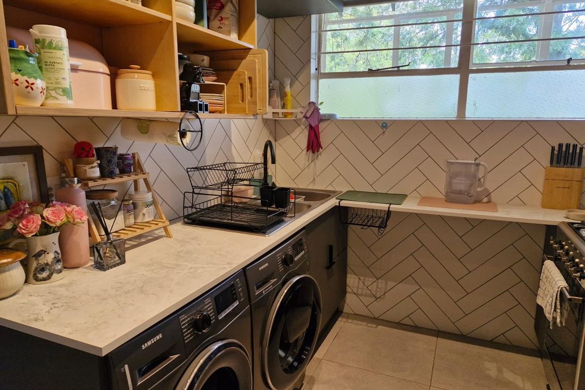 A functional kitchen featuring herringbone tiled splashbacks, stone-look countertops, integrated laundry appliances, and open timber shelving.