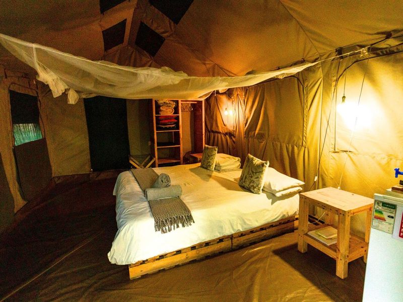A rustic safari-style bedroom tent featuring a canvas structure, integrated mosquito netting, and built-in storage shelving.