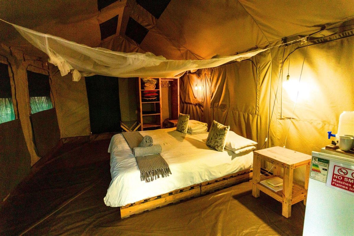 A rustic safari-style bedroom tent featuring a canvas structure, integrated mosquito netting, and built-in storage shelving.