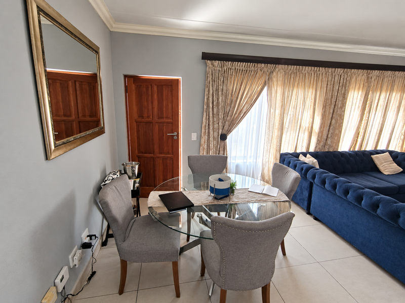 A well-maintained living area featuring tiled flooring, crown molding, and a solid timber door, with ample natural light through large window treatments.