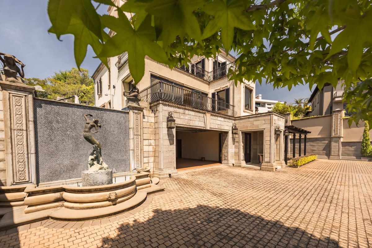 A well-maintained rear exterior featuring a stone-paved courtyard, an elegant water feature, and a multi-level facade with wrought iron balcony railings.