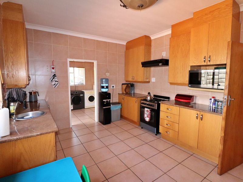 A functional kitchen featuring wooden cabinetry, granite countertops, tiled walls and flooring, with an adjacent laundry area visible through the doorway.