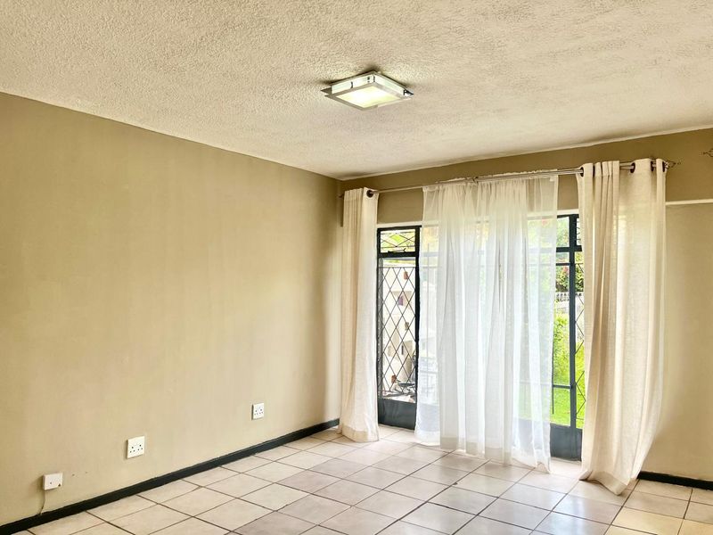 An empty living room featuring tiled flooring, a ceiling light fixture, and a sliding glass door with an integrated security gate.