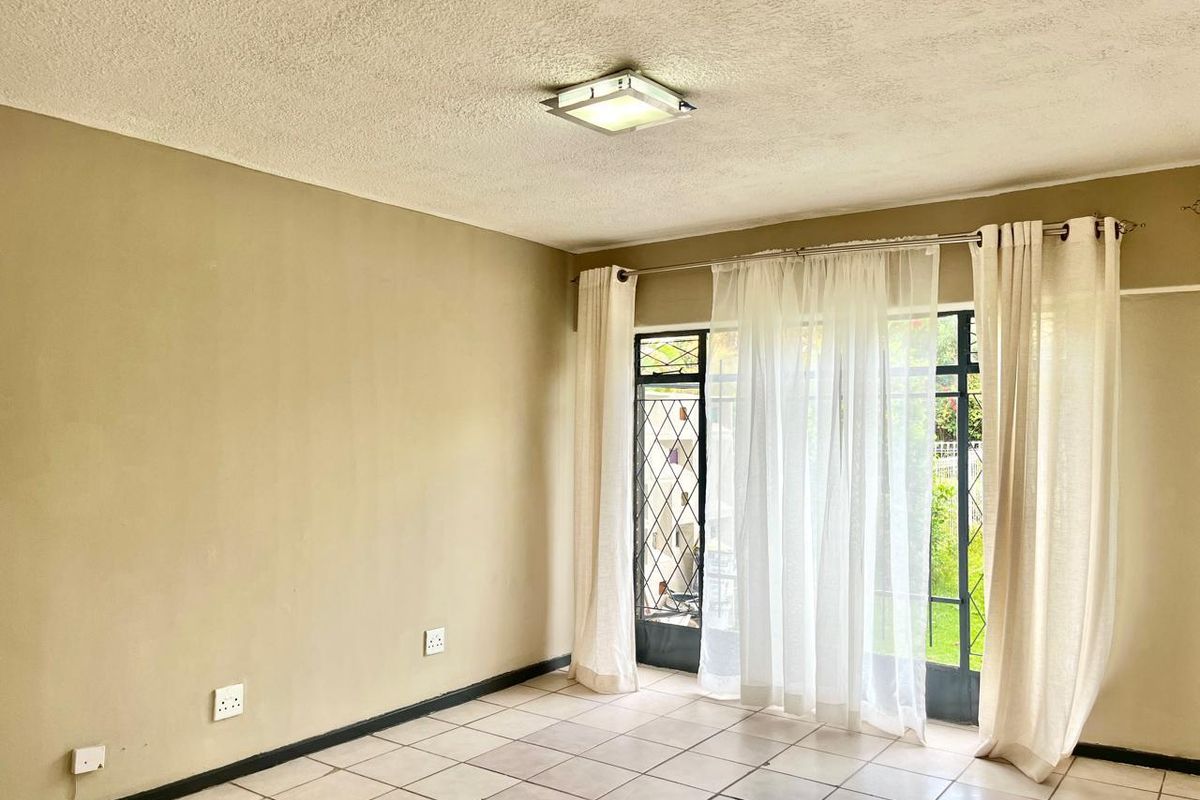 An empty living room featuring tiled flooring, a ceiling light fixture, and a sliding glass door with an integrated security gate.