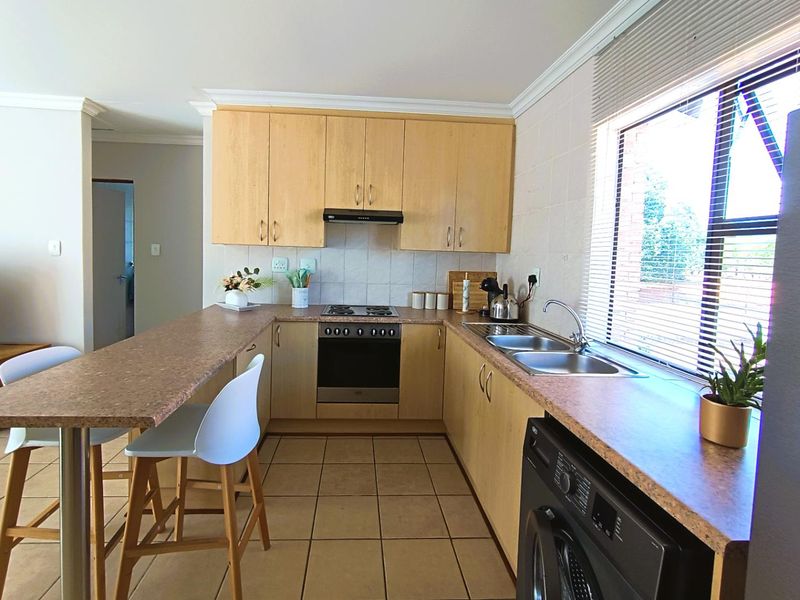 Functional kitchen featuring light wood cabinetry, laminate countertops, a breakfast bar, built-in oven with hob, and tiled flooring with a convenient laundry connection.