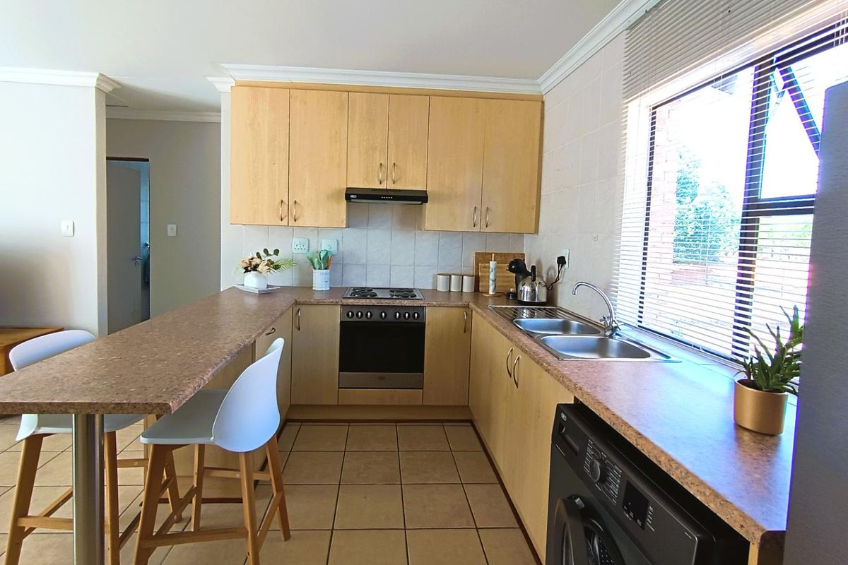 Functional kitchen featuring light wood cabinetry, laminate countertops, a breakfast bar, built-in oven with hob, and tiled flooring with a convenient laundry connection.