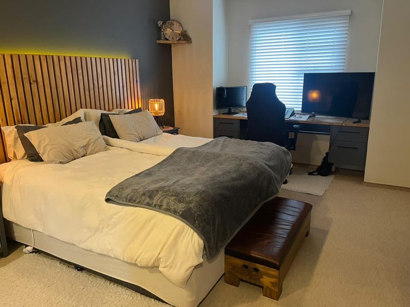 A well-maintained bedroom featuring a modern slatted timber headboard wall with integrated LED lighting and functional venetian blinds.