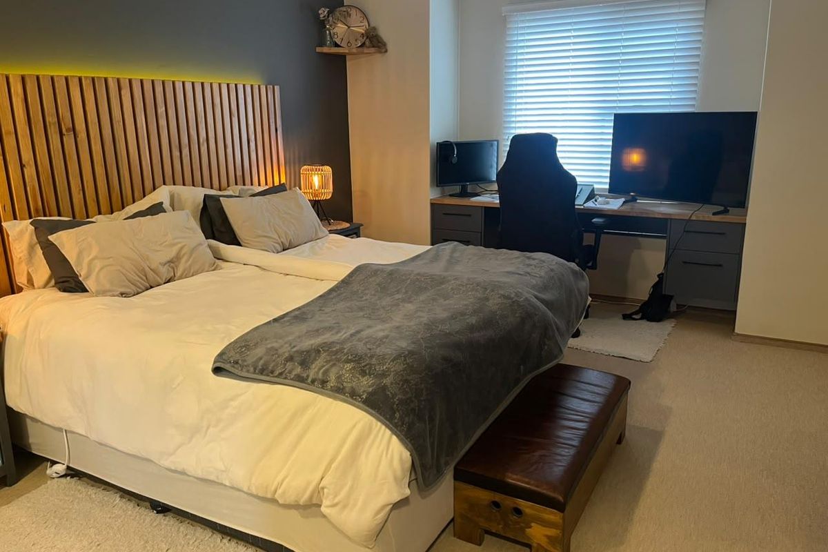A well-maintained bedroom featuring a modern slatted timber headboard wall with integrated LED lighting and functional venetian blinds.