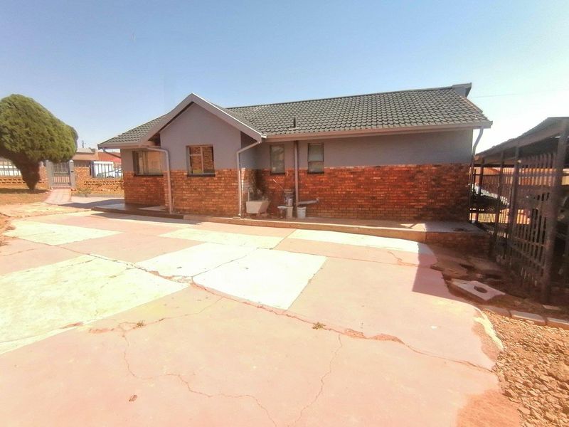 Rear view of a single-story house featuring a combination of brick and painted walls, a tiled roof, and a paved driveway area.