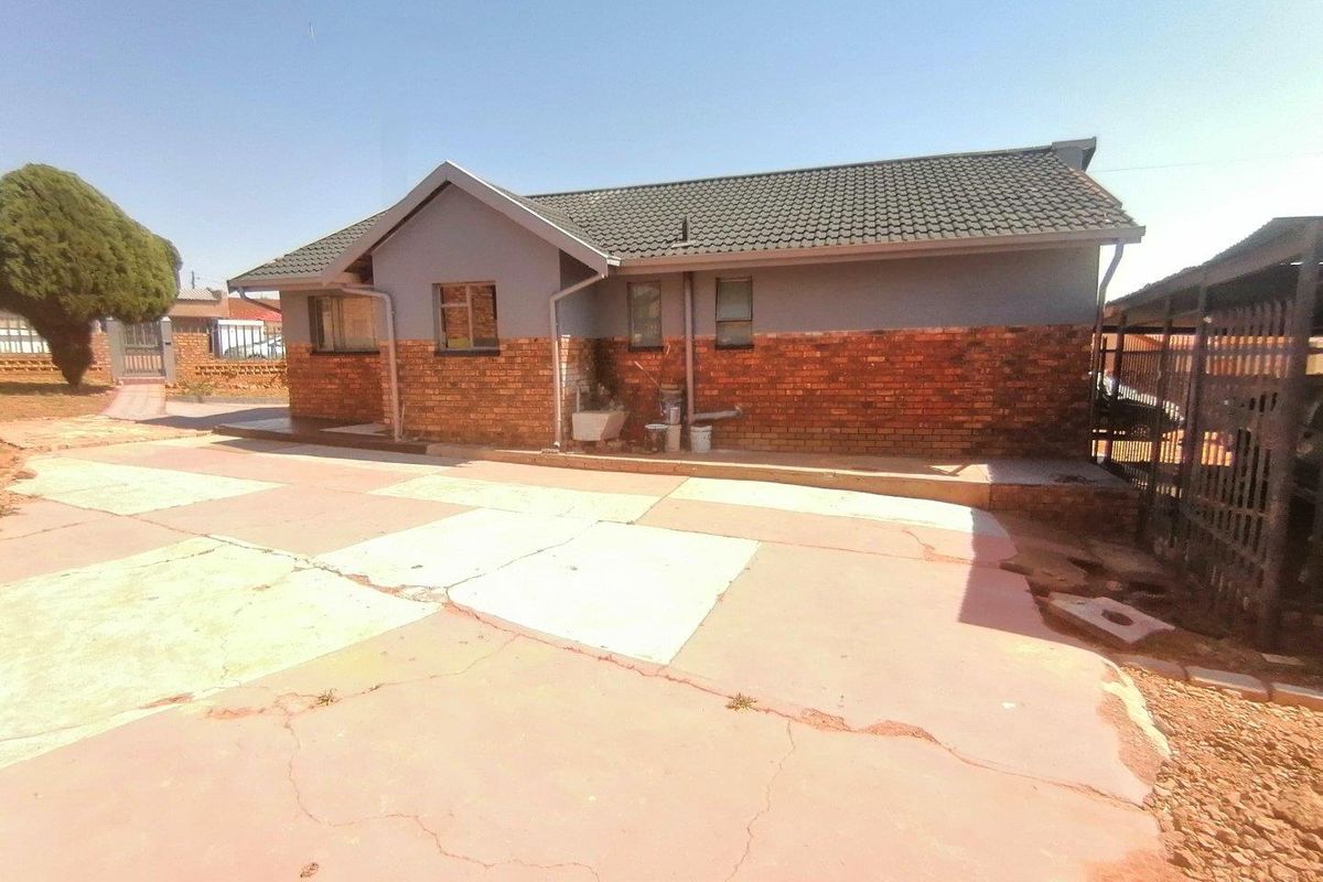 Rear view of a single-story house featuring a combination of brick and painted walls, a tiled roof, and a paved driveway area.