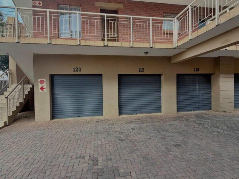 A row of numbered garage units with roller shutter doors, featuring a paved driveway and an external staircase leading to the upper level.