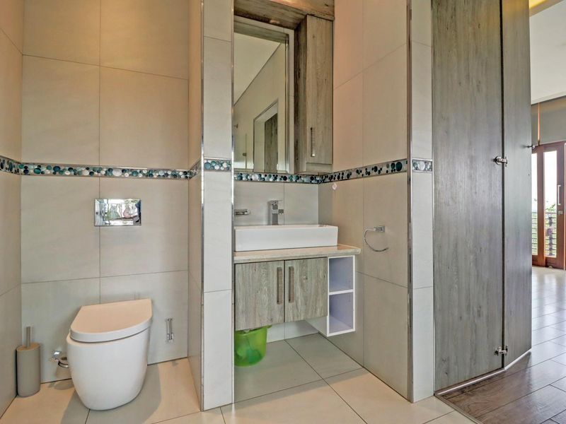 Modern bathroom featuring a wall-mounted toilet, vessel sink with vanity cabinet, and neutral tiled finishes with a decorative mosaic accent border.