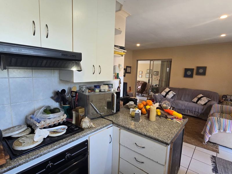 Open-plan kitchen and living area featuring built-in cabinetry, granite countertops, and tiled flooring, providing a functional layout with direct access to the living space.