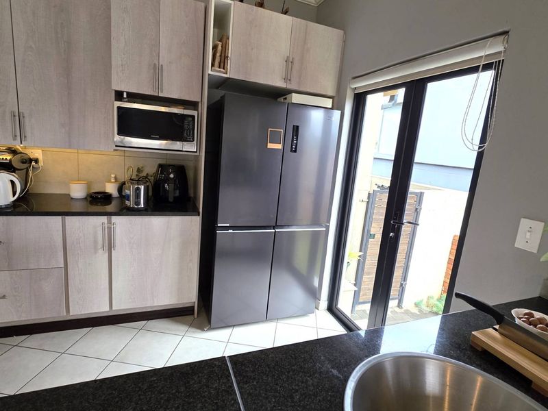 Modern kitchen featuring light wood-grain cabinetry, dark granite countertops, built-in microwave, and direct access to the exterior through a glass door.
