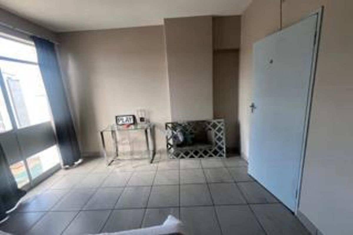 A simple living area featuring tiled flooring, a large window with curtains, and a standard interior door.