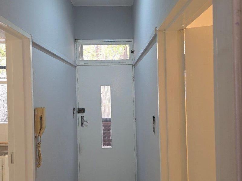 A clean, functional hallway featuring tiled flooring, a transom window above the door, and a wall-mounted intercom system.