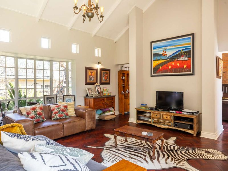 Spacious living room featuring a high vaulted ceiling, rich herringbone timber flooring, and large multi-pane windows that provide ample natural light.