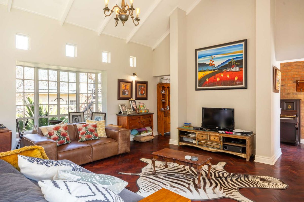 Spacious living room featuring a high vaulted ceiling, rich herringbone timber flooring, and large multi-pane windows that provide ample natural light.
