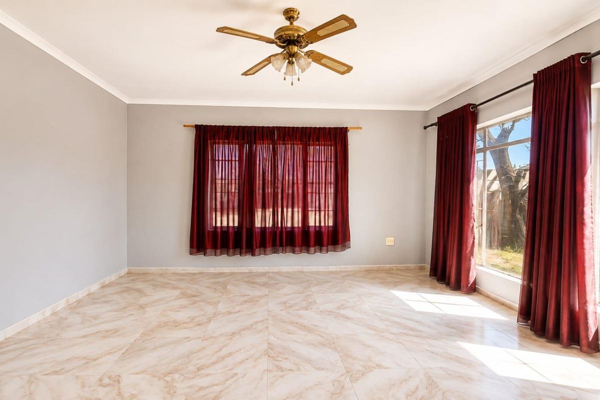 A bright, empty living room featuring neutral tiled flooring, a ceiling fan, and large windows that provide ample natural light.