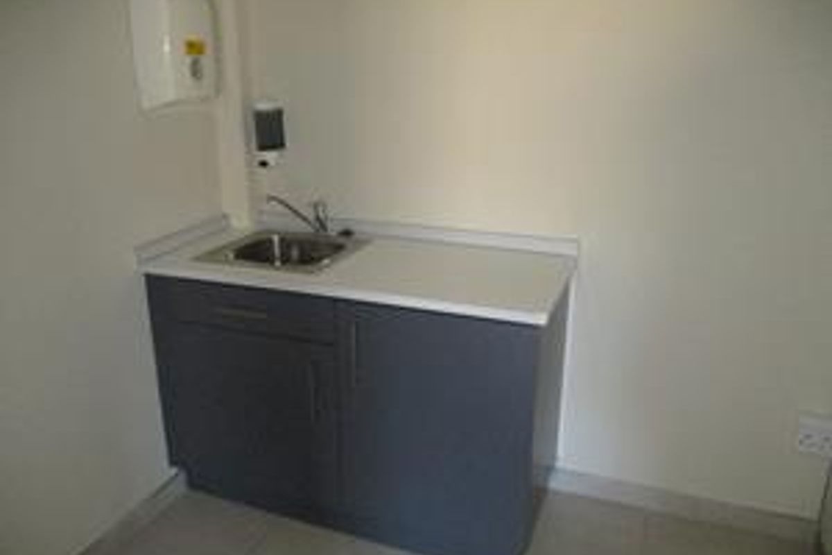 A functional utility space featuring a compact base cabinet with a stainless steel sink, countertop, and wall-mounted hygiene dispensers.