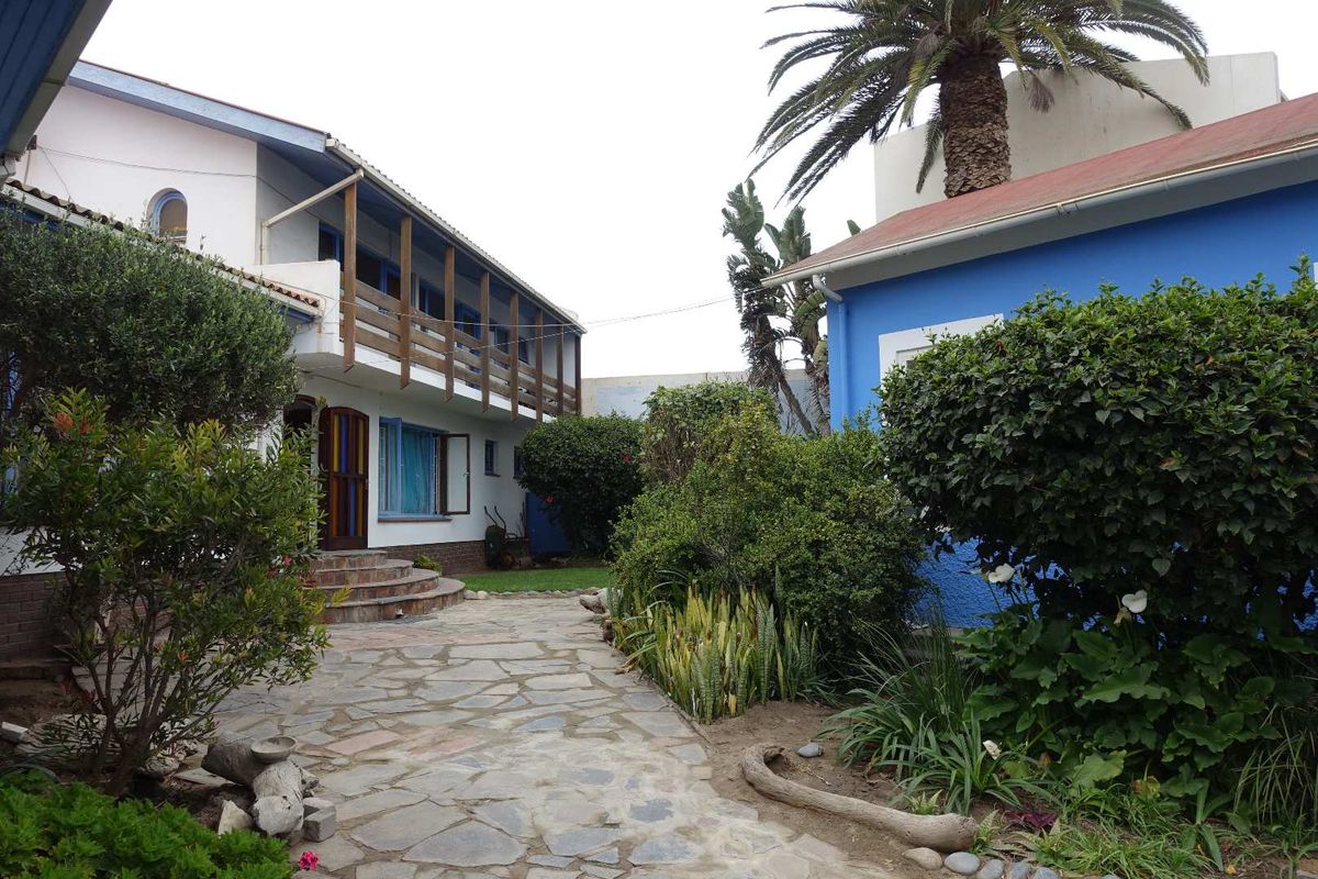A courtyard garden area featuring a stone-paved pathway between two building structures, including a two-story building with a wooden balcony.