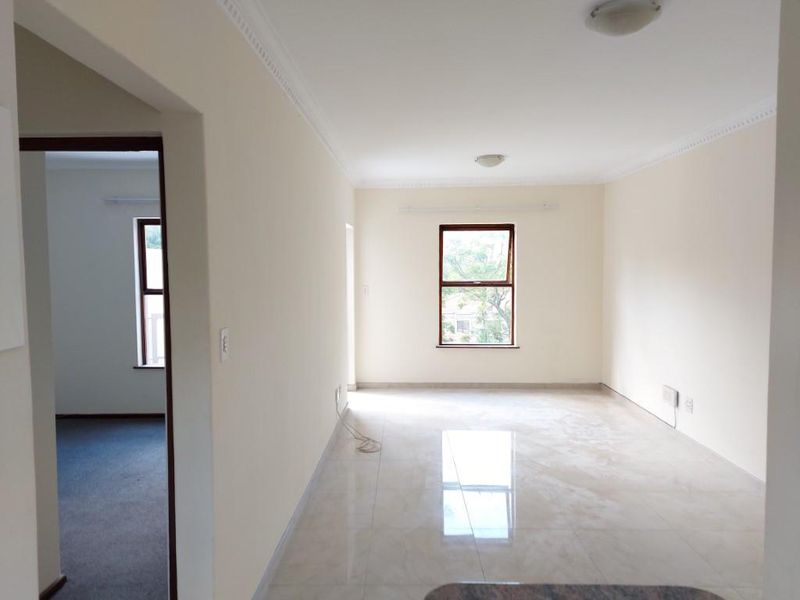 A bright, empty living area featuring neutral tiled flooring, clean walls, and ceiling cornicing, offering a versatile space for interior design.