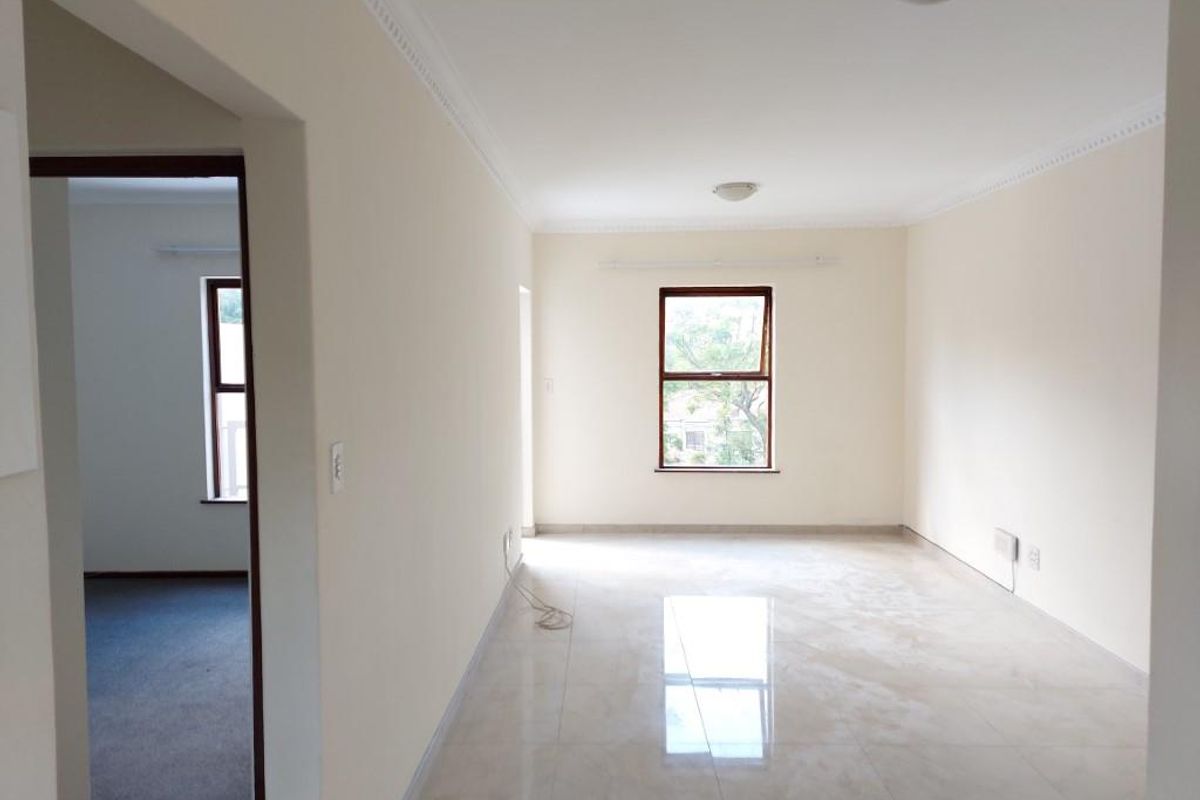 A bright, empty living area featuring neutral tiled flooring, clean walls, and ceiling cornicing, offering a versatile space for interior design.