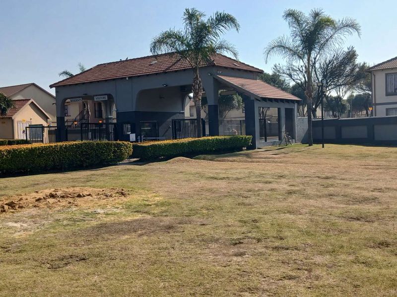 View of the apartment complex security entrance and gatehouse with surrounding landscaped grounds and perimeter walling.