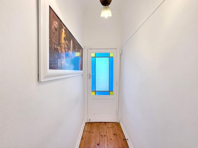 A bright, clean hallway featuring polished timber flooring and a classic white door with decorative stained glass inserts.